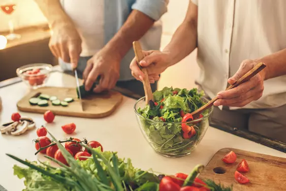 two sets of hands chopping and mixing up a salad on a kitchen counter