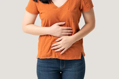 woman in orange t-shirt and blue jeans holding both hands to her stomach.