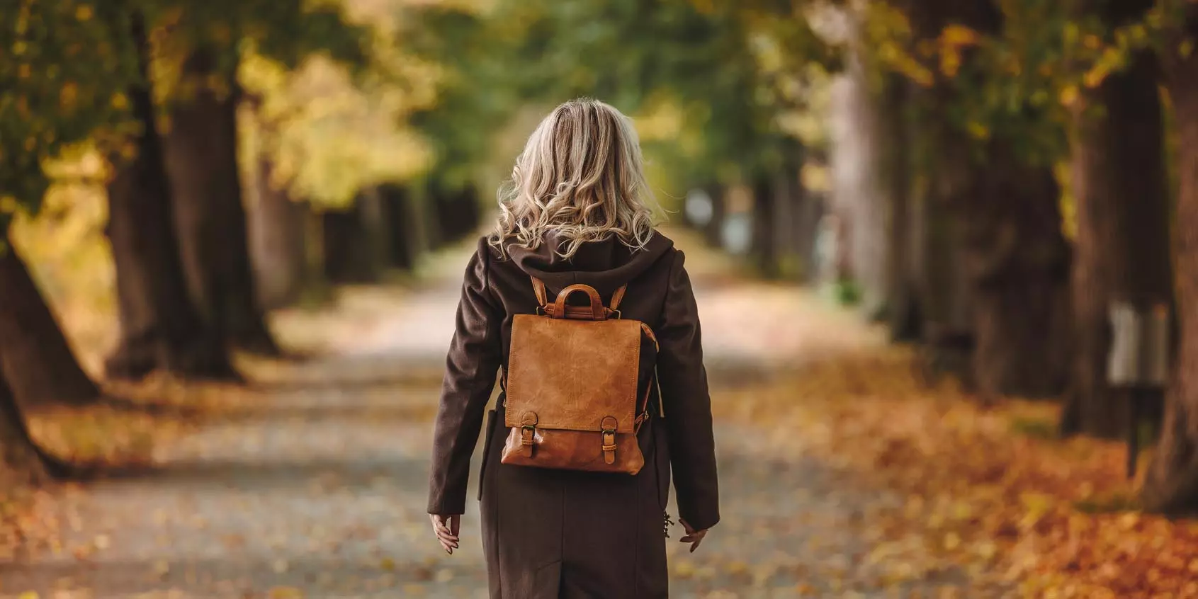 a woman with a leather backpack walking away from the camera