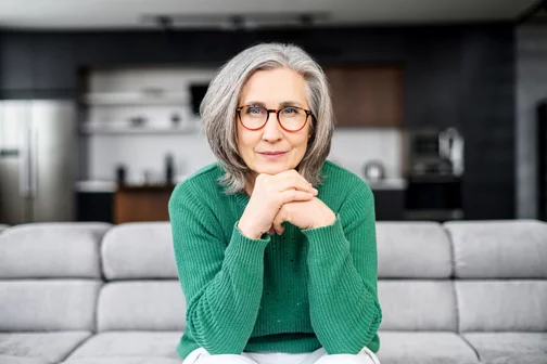 older woman with silver hair, red glasses, and a green top looking right at the camera.
