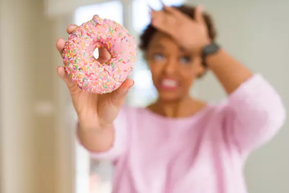 woman fighting cravings while holding donut