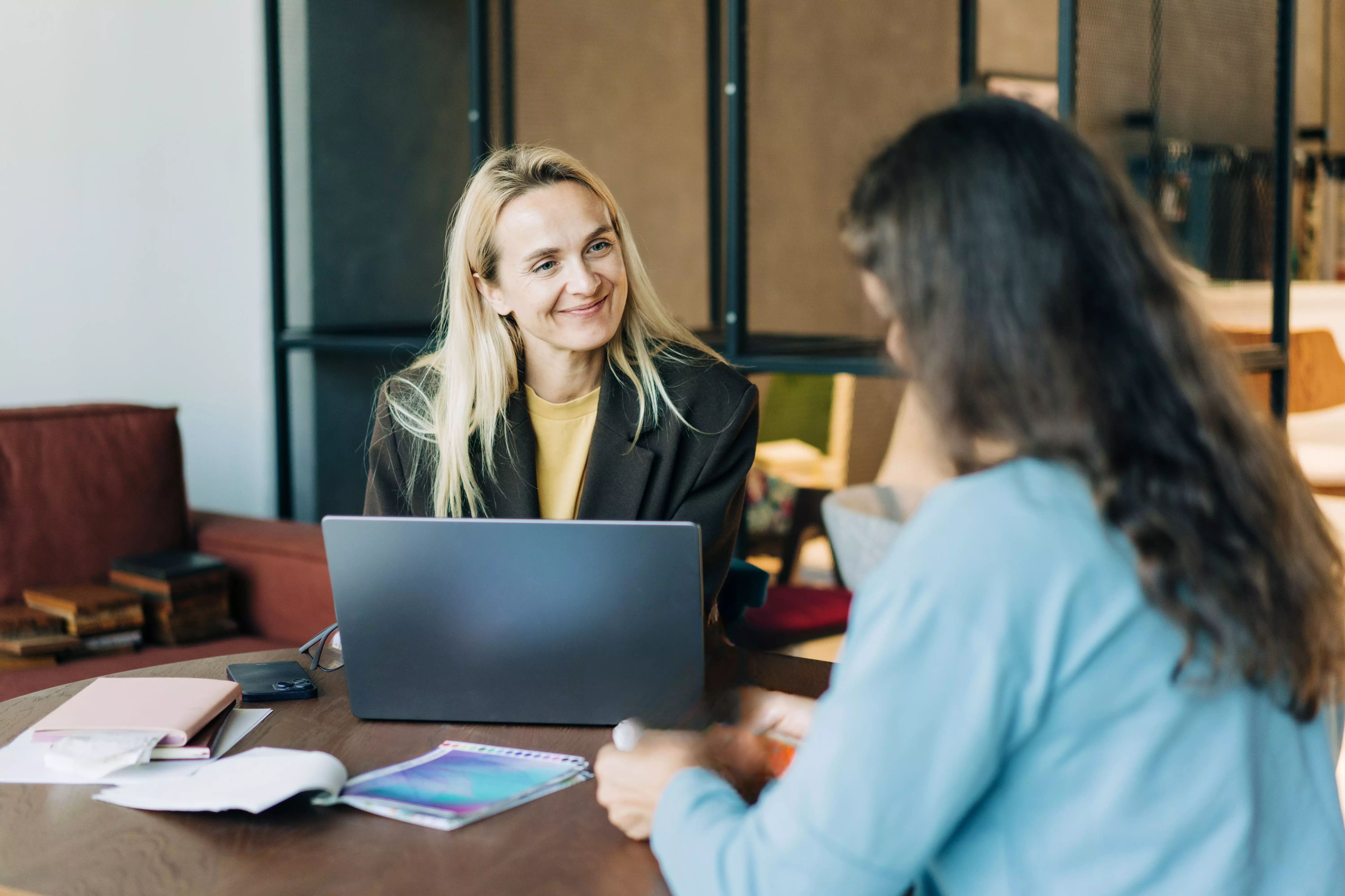 a woman with a computer smiling and looking across the table to another woman